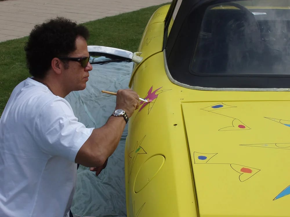 L’artiste au travail sur la carrosserie, pinceau à la main.