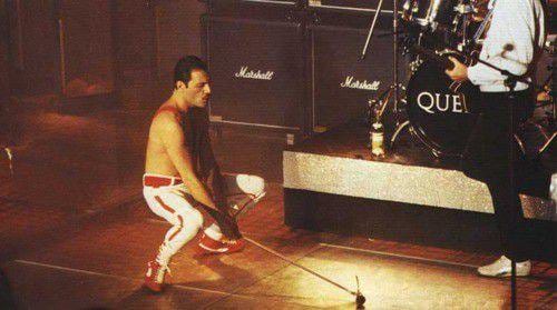 Freddie Mercury accroupi sur scène, devant la batterie de Roger Taylor, à la Rose d’Or, en 1984.