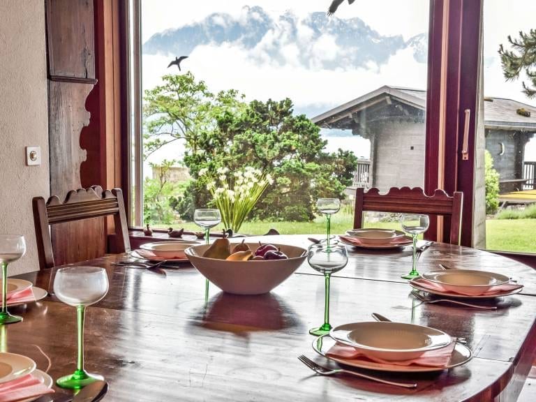 La table dressée devant la baie vitrée, ouverte sur le jardin, le chalet et les montagnes.