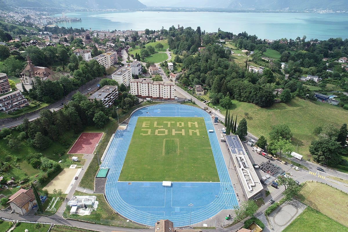 Le stade de la Saussaz, terrain de football de Montreux, préparé pour l’événement : le nom d’Elton John est dessiné sur la pelouse, face au lac et aux Alpes.